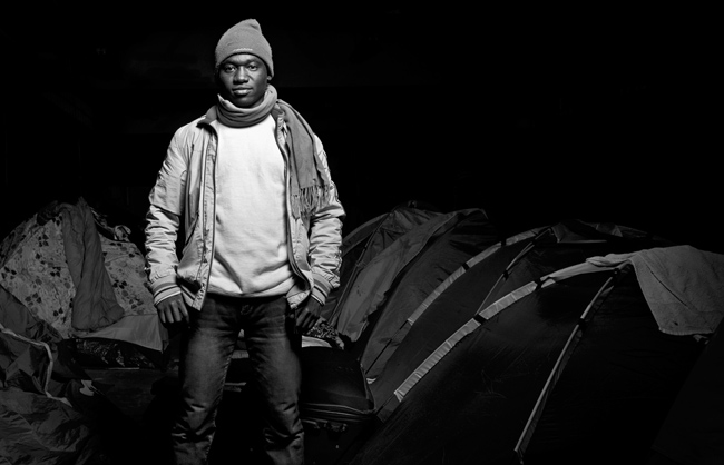 A young Sudanese Refugee posing in front of his tent in the 'Tioxide Jungle' of Calais while waiting for the good moment to cross the sea and reach his 'Promised Land' in the United Kingdom. (Calais - France - 2014)