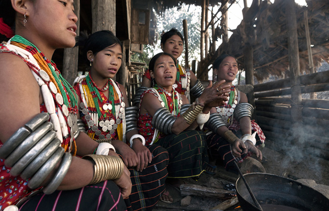 Early on the morning, Pangmi Naga women from Hachi, weighed down by their heavy armbands, warm them up around the woodfire. Round their necks the Hachi women have necklace chain of old coins and tubular shells.