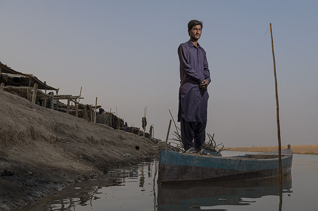 Portrait of Bashir aboard a Hurro, the traditional slender boat. In the background, the simple huts on the raised banks of the Right Bank Outfall Drain (RBOD) are a testament to a precarious life. His dream would be to build a brick house for himself and his family.