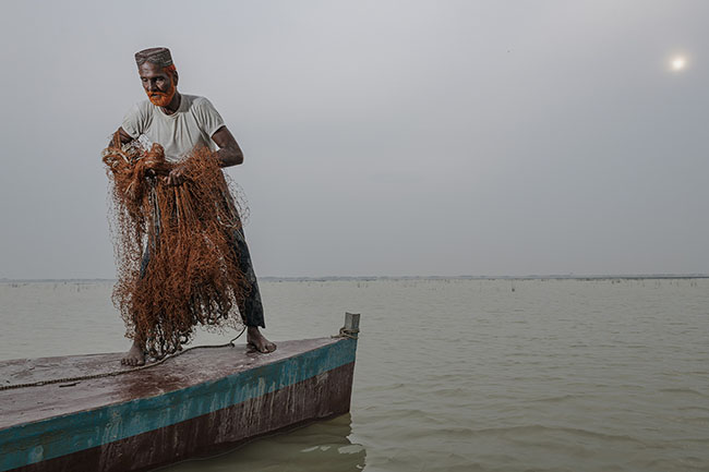 Mohamed prepares to cast his net into the water. Only the oldest Mohanas still know how to use this technique, now almost forgotten. Once, nearly every cast would bring fish. Today, even after hours of fishing, he often returns empty-handed.