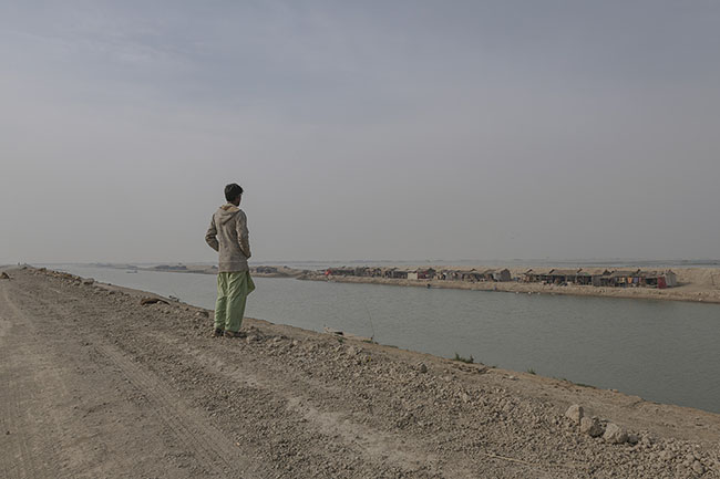 Bashir gazes at the few huts standing on the opposite bank of the Right Bank Outfall Drain (RBOD), where he and his family have now settled on land.