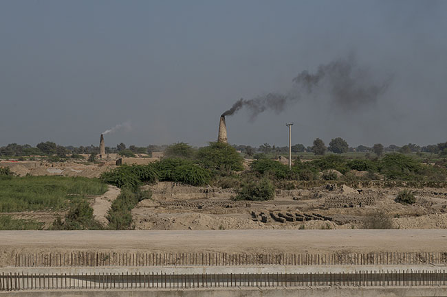 Black smoke rises from a brick kiln. The brick kiln owners, like the landowners, exert significant control over the vast agricultural plains of Sindh, to the detriment of workers and the environment. This unregulated sector contributes massively to air pollution, and consequently to climate change, which directly impacts the lives of the Mohanas.