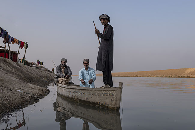 Portrait of three Mohana aboard a Hurro, the traditional boat. In the background, the rudimentary huts on the raised banks of the Right Bank Outfall Drain (RBOD) testify to a precarious life.